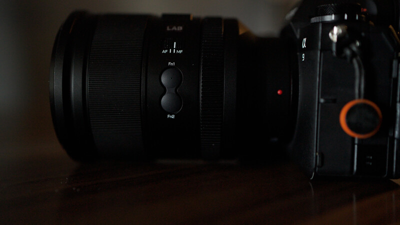 Camera lens with manual focus ring and depth of field scale mounted on black camera body with orange accents.