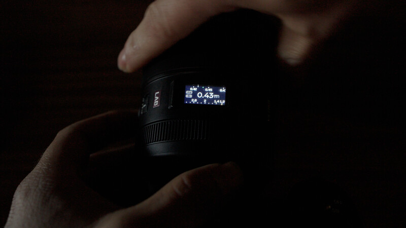 Close-up of a camera lens with an illuminated LCD display showing autofocus distance of 0.43m.