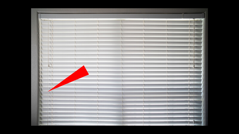 Red paper cone casting a shadow on white horizontal blinds in natural light.