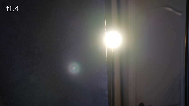 Bright light source creating lens flare and glare against dark background at f1.4 aperture.