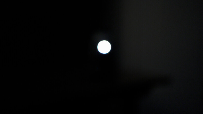 Bright white circular light source centered against a dark, shadowed background.