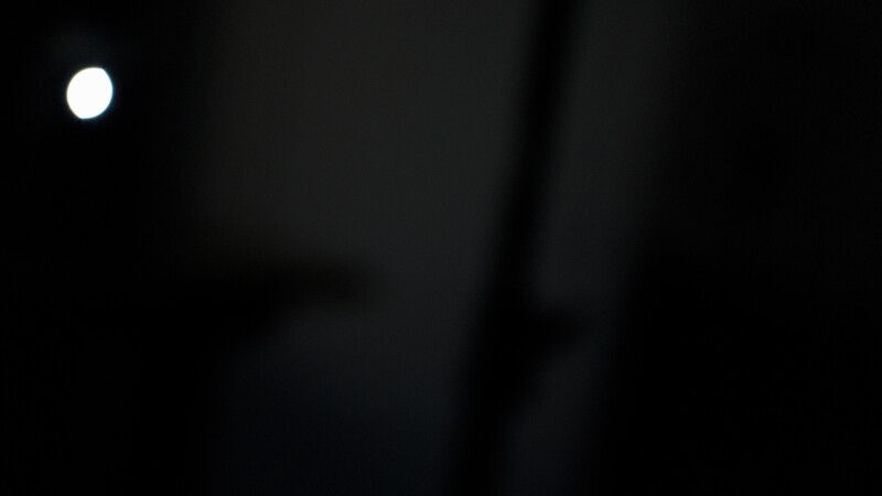 A bright white circular light source in the upper left corner against a predominantly dark, black background.