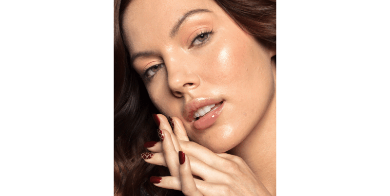 Woman with glowing skin touching her face, eyes downcast in soft lighting.