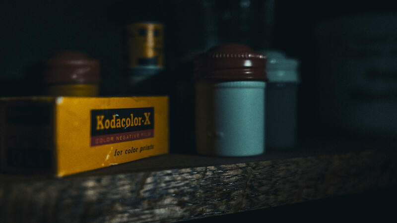 Vintage Kodacolor-X film box and film canisters arranged on weathered wood surface.
