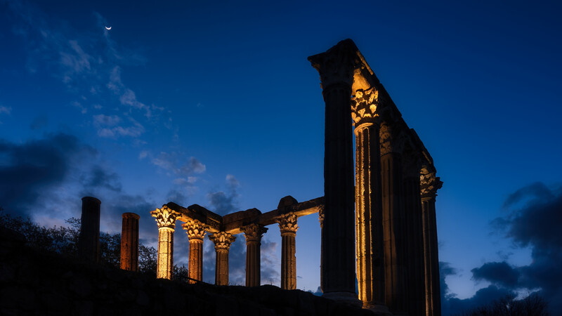 A roman ruin photographed at blue hour with the moon in the sky