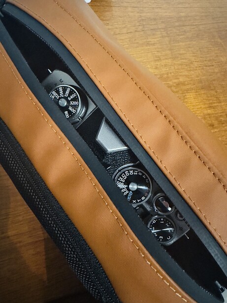 Camera strap with analog gauge dials and aperture markings printed on black fabric, laid against tan leather.
