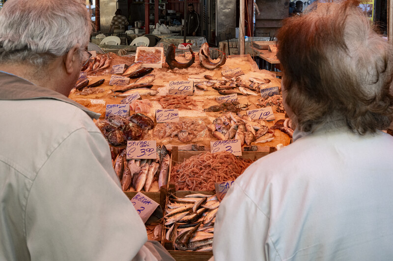 Two people viewing a wooden sculpture display with carved figures and objects arranged on an orange-brown surface.