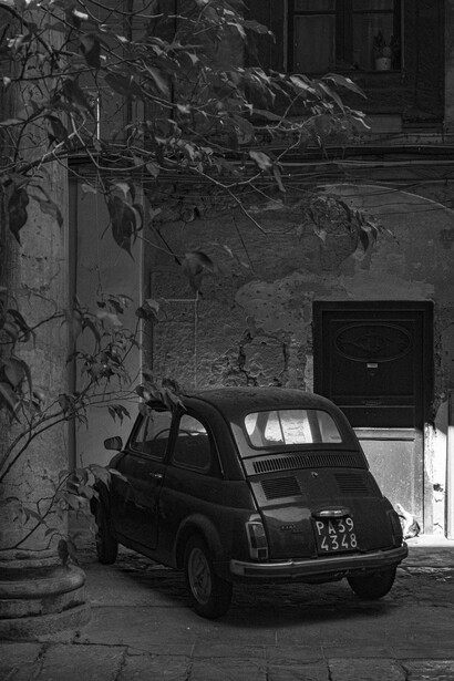 Vintage Fiat 500 parked against a weathered building wall with climbing ivy in black and white.