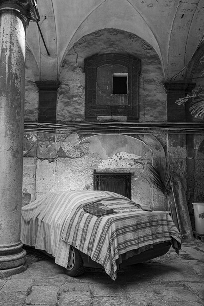 Striped bed in a deteriorating stone room with arched ceiling and supporting columns.