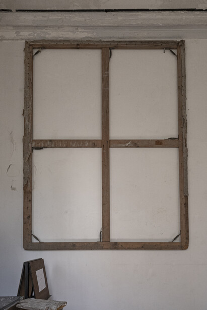 Weathered wooden window frame with four panes mounted on a white wall.