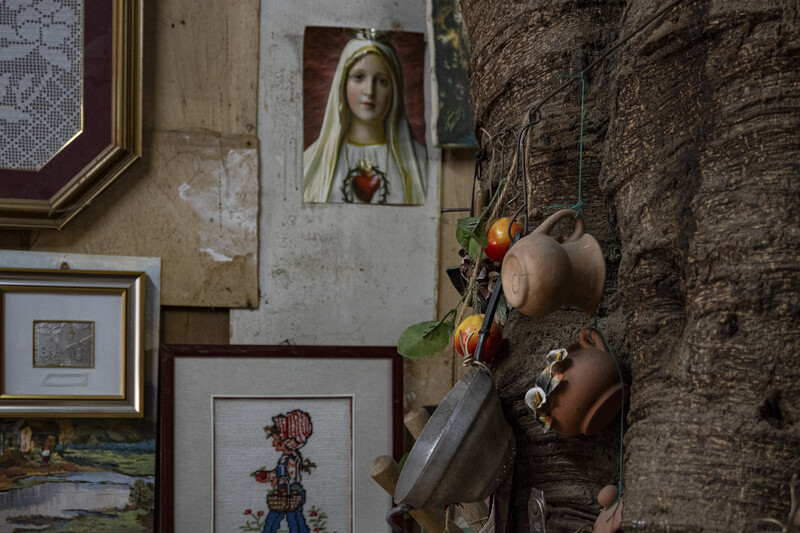 Weathered stone wall displaying framed artwork, religious imagery, and clay pottery vessels.