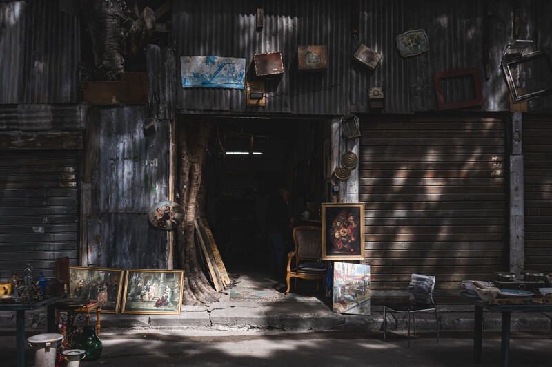 Weathered industrial storefront with open metal door and scattered artwork leaning against corrugated walls.