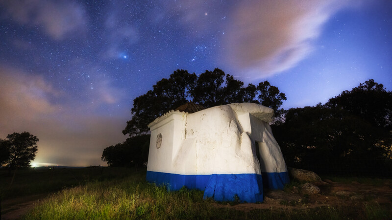 A partly cloudy night sky with the constellation Orien above a dolman in the Portuguese country side.