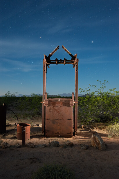 Rusted metal structure with wooden posts against desert landscape under blue sky.