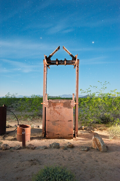 Rusty metal structure with triangular roof frame standing in arid desert landscape under clear blue sky.