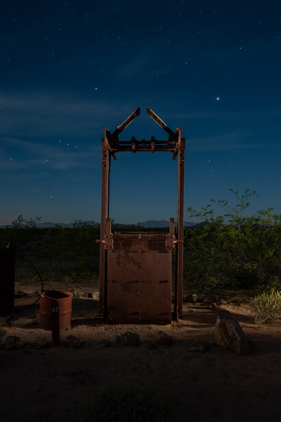 Abandoned metal structure silhouetted against a starry night sky in an arid landscape.