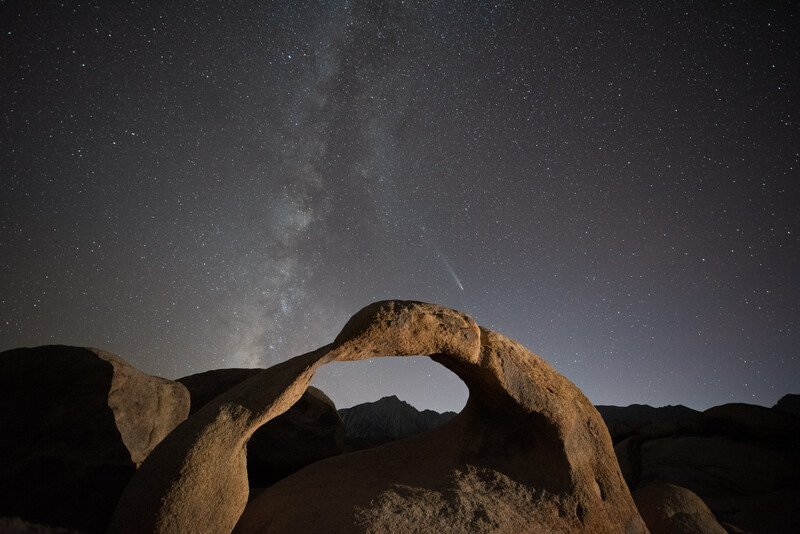 Natural rock arch frames the Milky Way and a meteor streaking across the night sky.