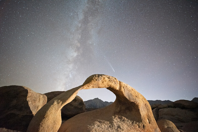 Natural rock arch framing a distant peak under the Milky Way and starry night sky.