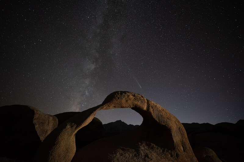 Natural rock arch framing the Milky Way galaxy under a starry night sky.