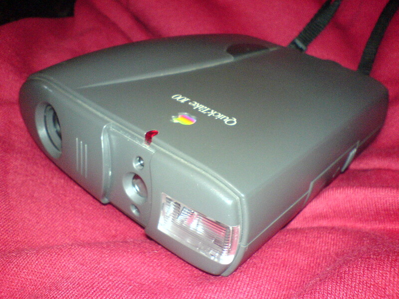 Vintage compact camera with gray body and red power indicator on pink fabric surface.