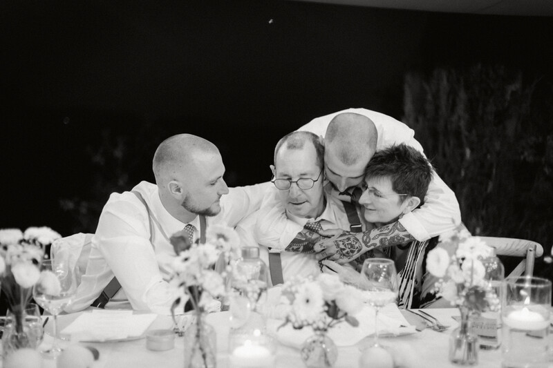 Four people in formal attire engaged in conversation at a dinner table with floral centerpieces.