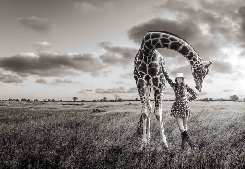 Woman leaning in a giraffe in a field.