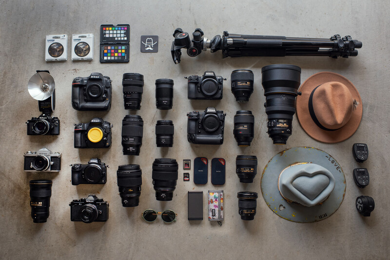 Flat lay of professional photography gear including multiple DSLR cameras, lenses, tripod, flash, memory cards, and accessories.