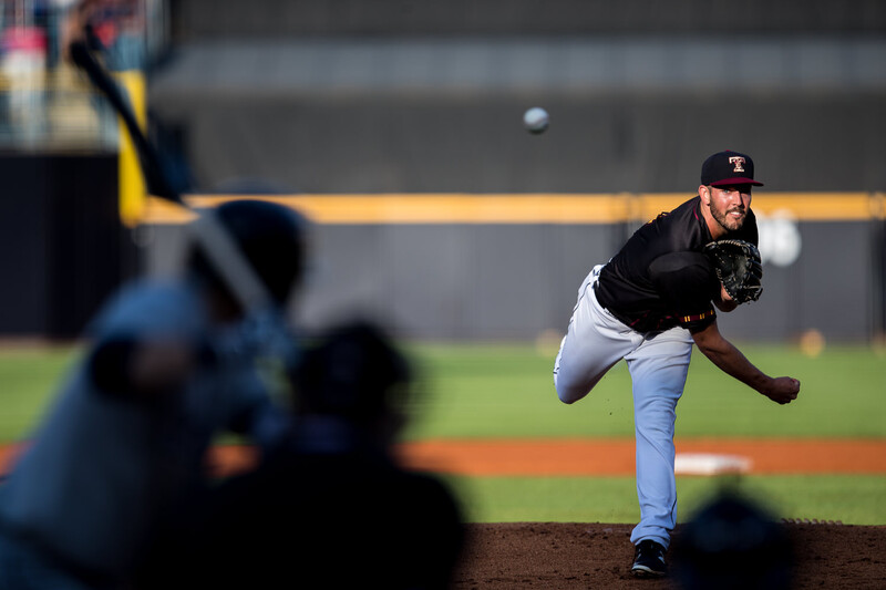 Baseball pitcher in mid-delivery, captured mid-throw with ball visible overhead during game.