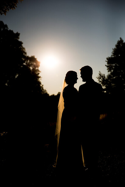 Silhouetted couple standing together against bright sun and trees during golden hour.
