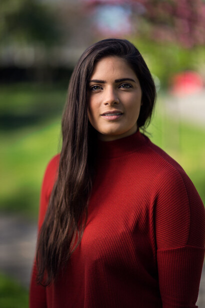 Woman in red sweater photographed outdoors with soft, blurred green background.