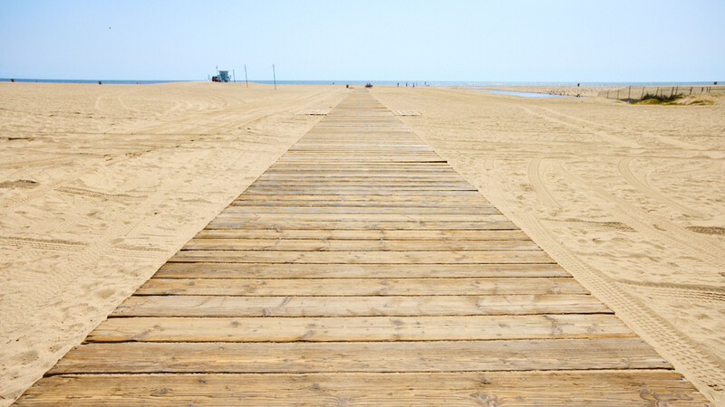 Wooden boardwalk stretching across flat sandy beach toward distant horizon.