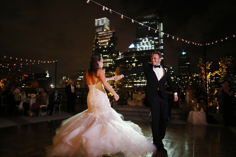 Bride and groom dancing during their first dance at an outdoor rooftop wedding reception at night.
