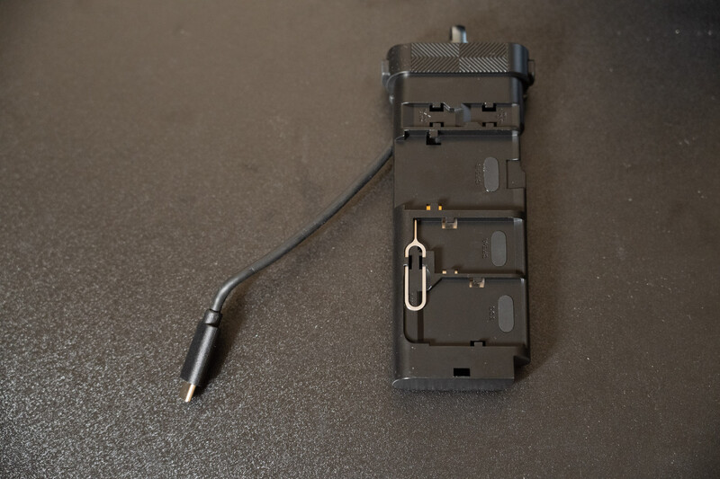 Black camera battery holder with three battery compartments and detached cable with connector.