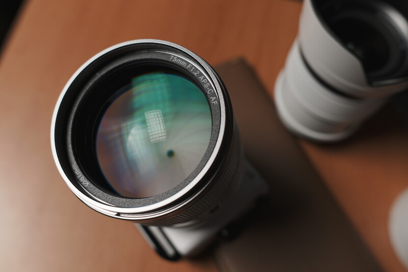 Close-up view of a telephoto lens front element showing internal optical glass and reflections on a wooden surface.