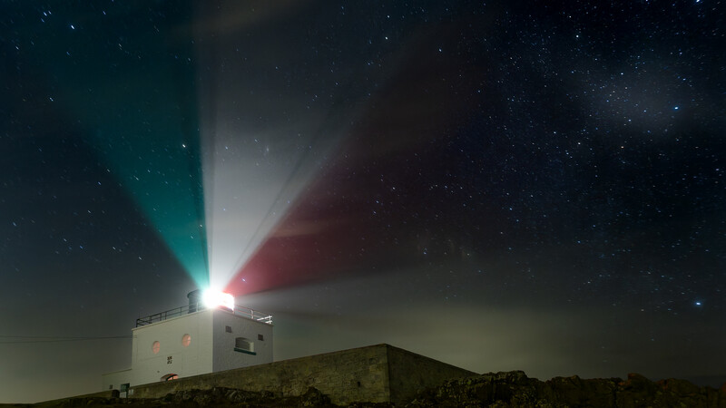 Lighthouse beam splitting into teal and red rays against a starry night sky.