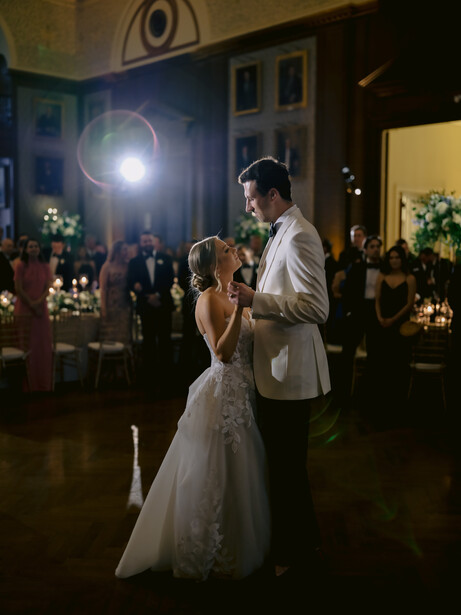 Bride and groom share their first dance at an indoor wedding reception illuminated by dramatic spotlight lighting.