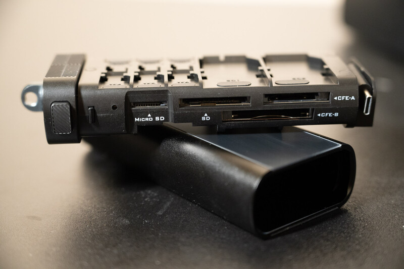 Camera external battery pack with memory card slots and USB ports displayed on dark surface.