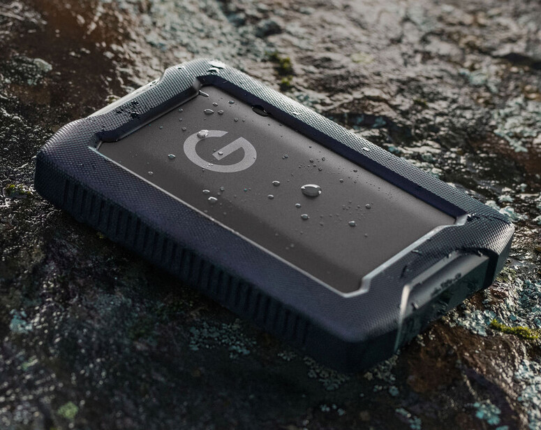 Rugged waterproof external hard drive with protective rubber casing on a moss-covered stone surface.