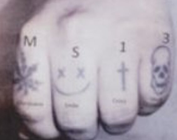 Close-up of four fingers with letters M, S, I, and number 3 tattooed on knuckles.