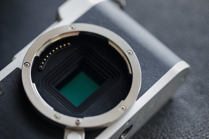 Camera body with open mirror box and sensor visible, showing electronic contacts on the interior mirror housing.
