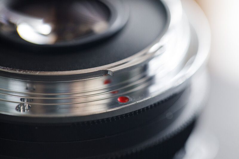 Close-up of camera lens mount showing chrome bayonet ring and red alignment dots.