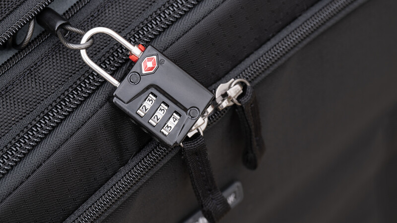 TSA-style combination padlock securing black camera bag zippers with metal carabiner attachment.