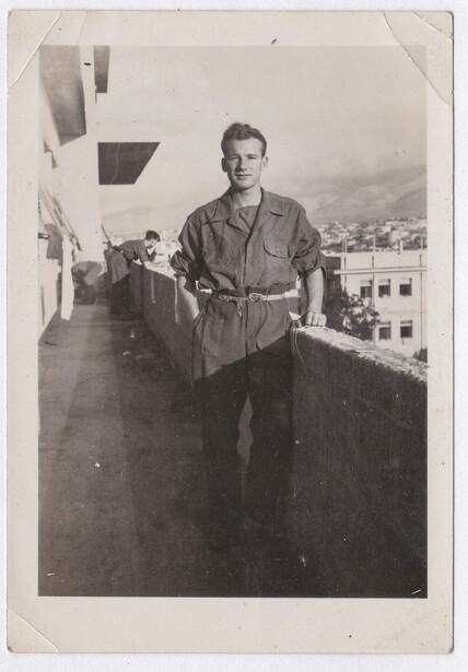 Man standing on a rooftop overlooking a mountainous cityscape, circa mid-20th century.