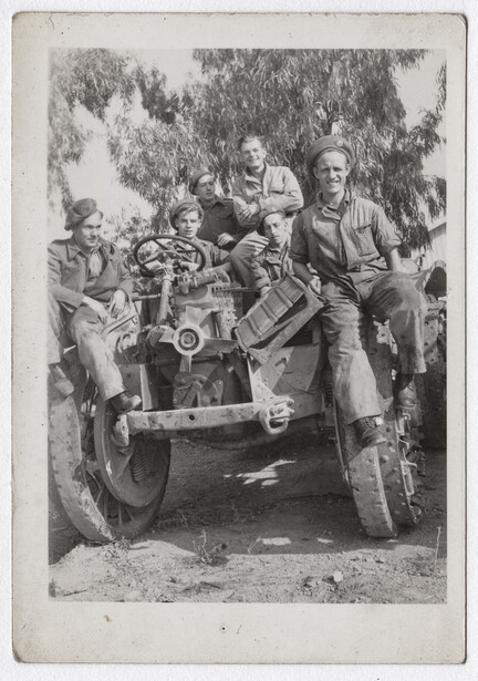 Group of seven men posed around and on top of an early automotive vehicle with large wheels.