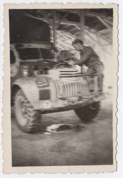 Man working on engine of vintage open-air vehicle in workshop setting.