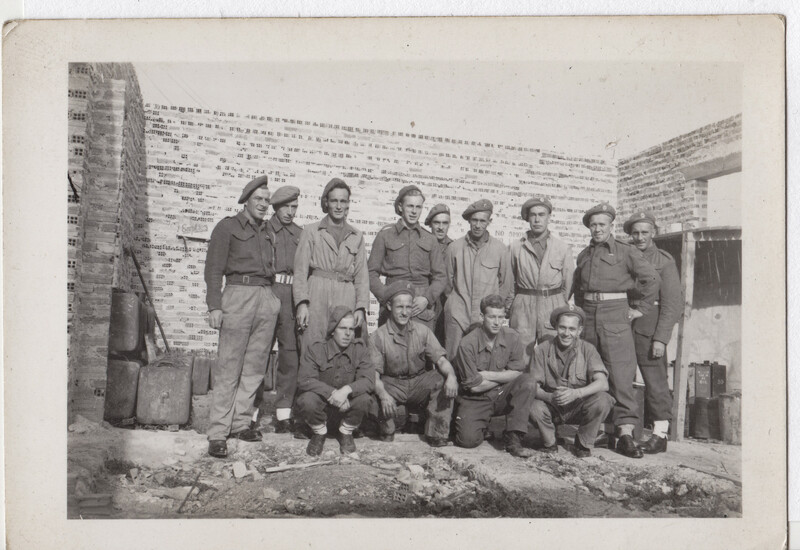 Group of uniformed workers posing against brick wall, with some standing and others crouched in front.