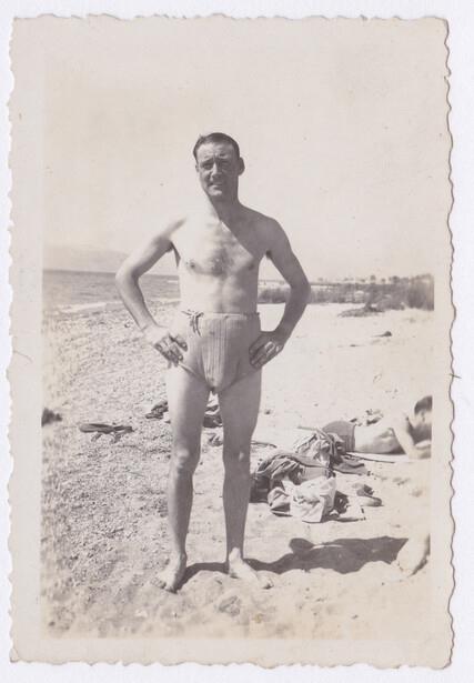 Shirtless man standing on a beach in a vintage black and white photograph.