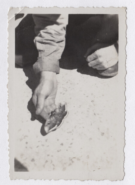 Two hands holding a small child's foot against sandy ground, shot from above in black and white.