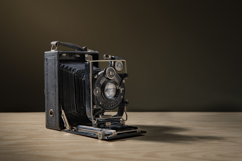 Vintage folding camera with bellows extended, displayed on wooden surface against dark background.