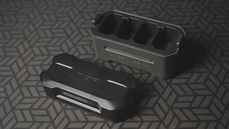 Two black battery chargers with compartmented charging docks displayed on a geometric patterned surface.